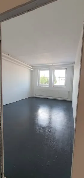 Renovierter Raum mit frisch aufgebrachter dunkler Bodenbeschichtung und hellem Fenster.