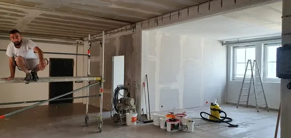 Innenraum während der Renovierung: Trockenbau, Gerüst, Werkzeug, helle Fensterfront.